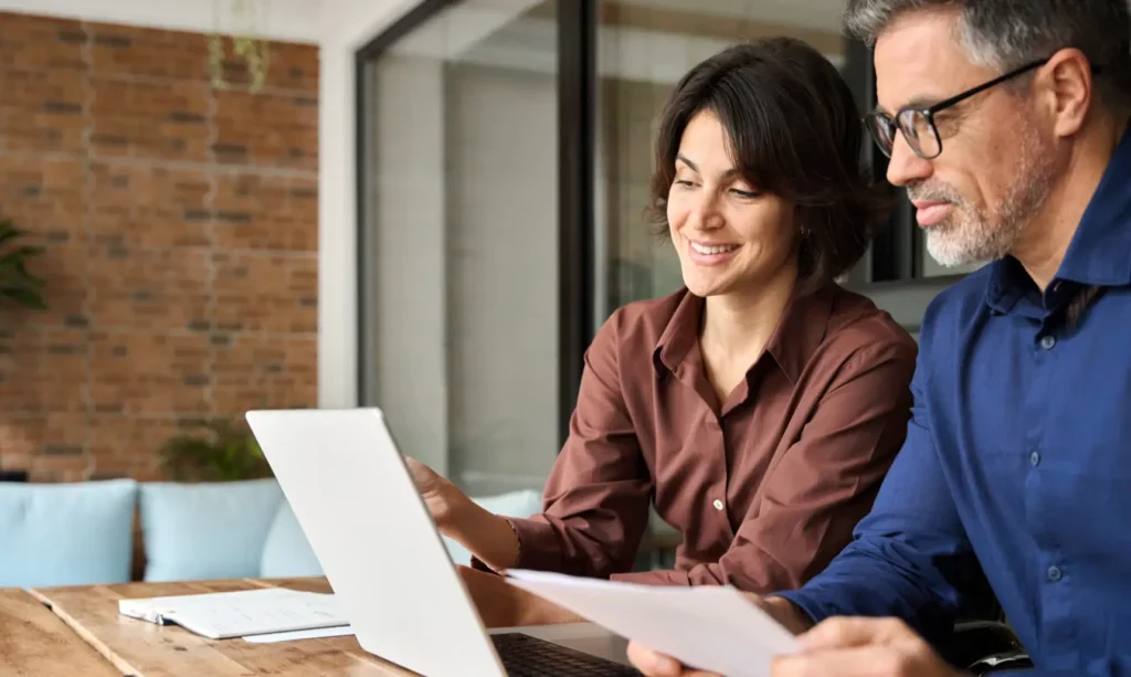 A businesswoman presenting clear recommendations on a laptop to a businessman, both engaged and collaborating in a professional office setting.