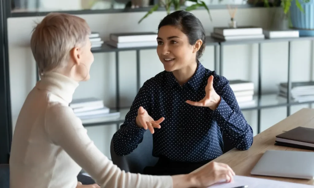 A professional woman actively addressing questions from a colleague in a collaborative office setting.